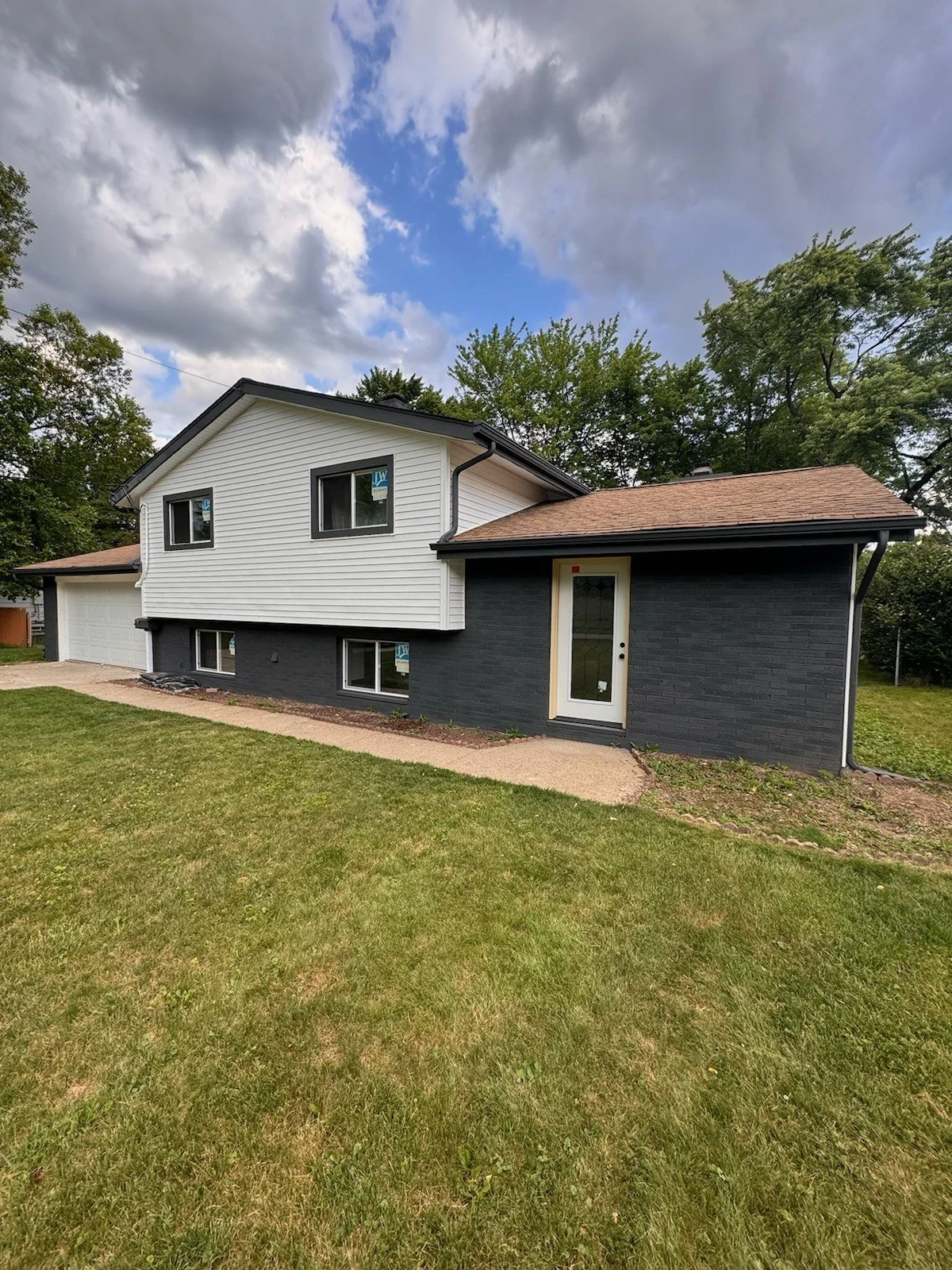Split-level exterior, after: front view from the lawn with light upper siding and dark charcoal lower walls.