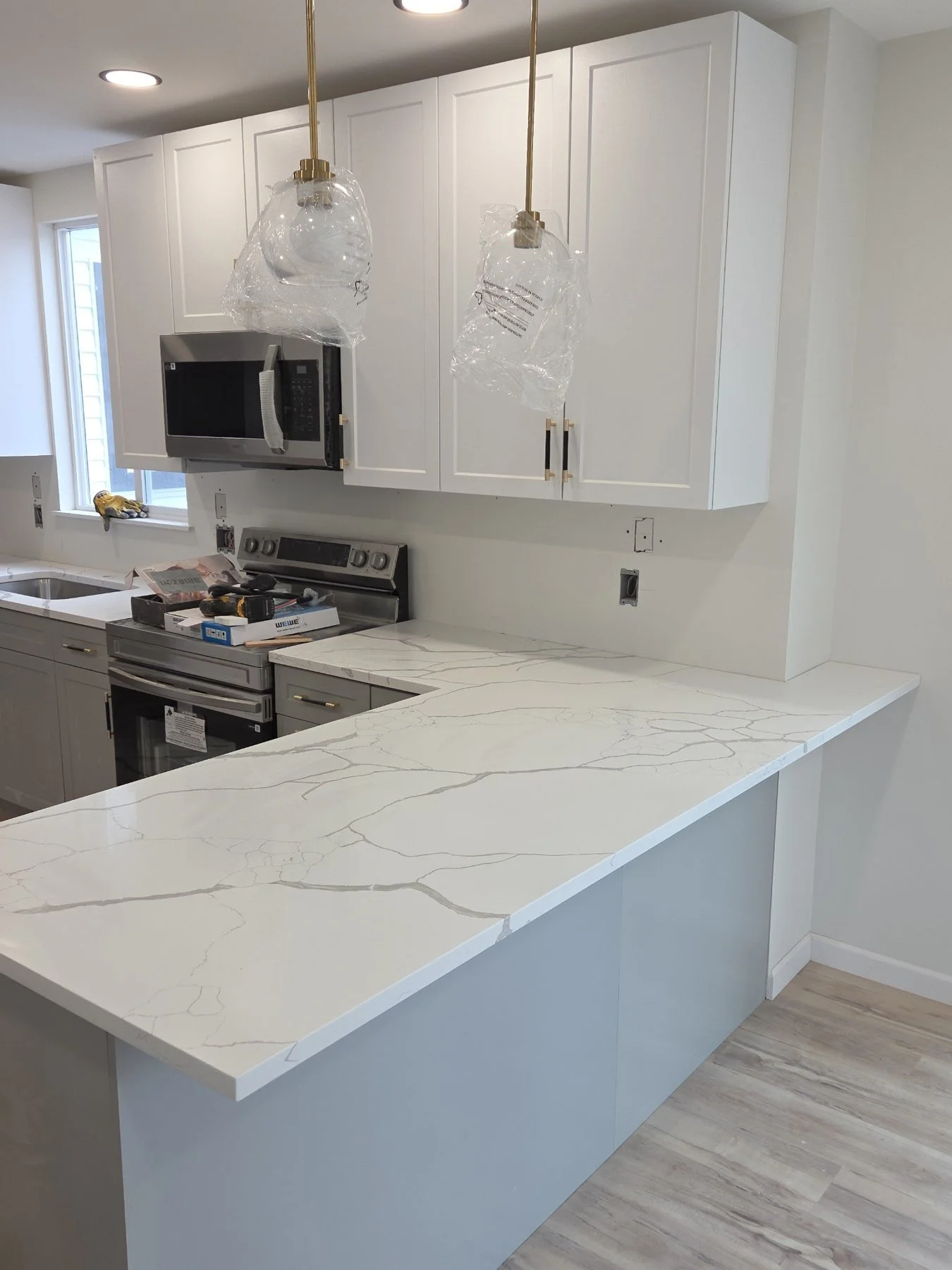 White kitchen cabinetry and veined peninsula countertop during final finishing