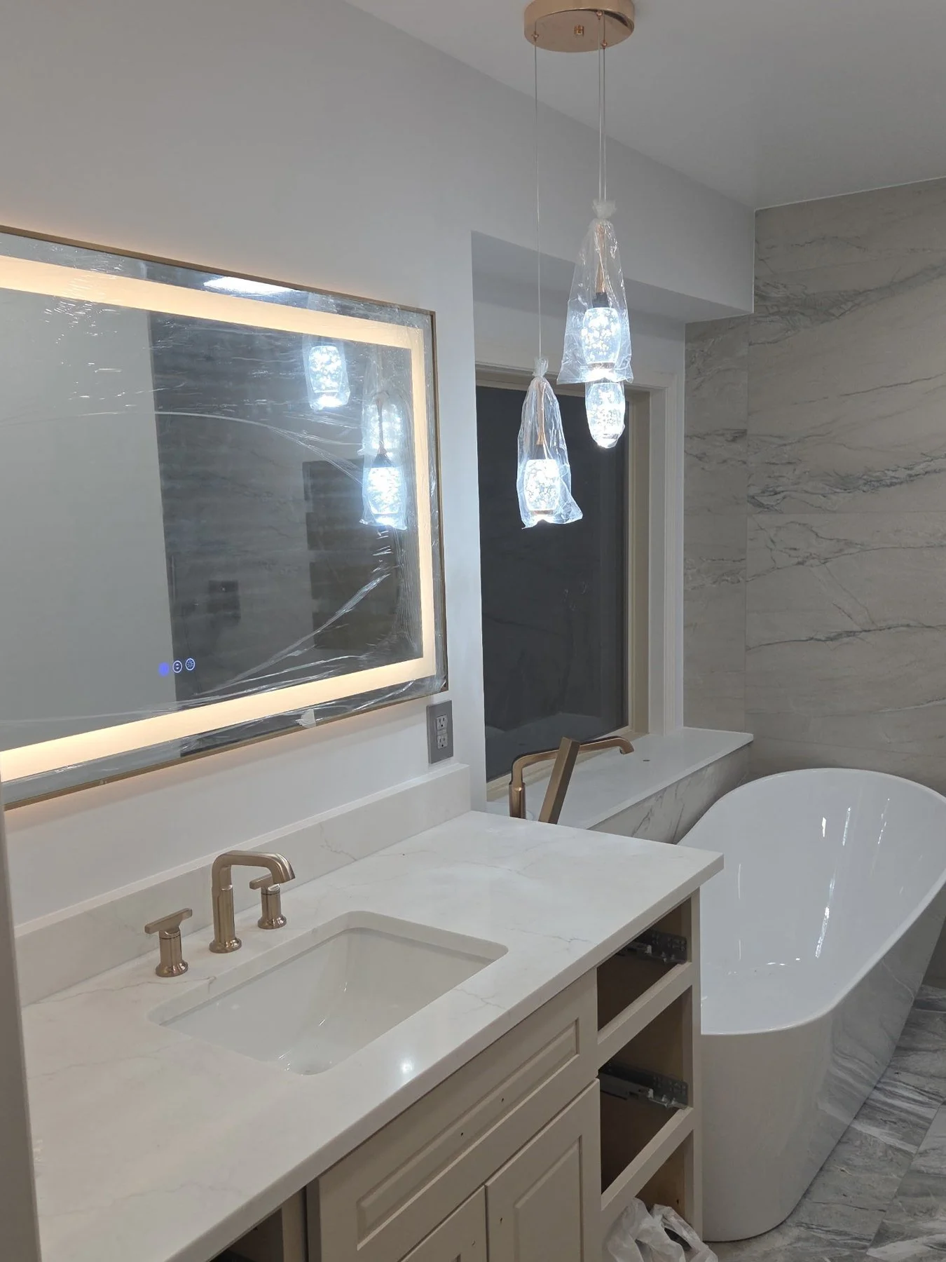 Bathroom vanity with a backlit LED mirror, gold fixtures, glass pendant lighting and marble-look floor tile.