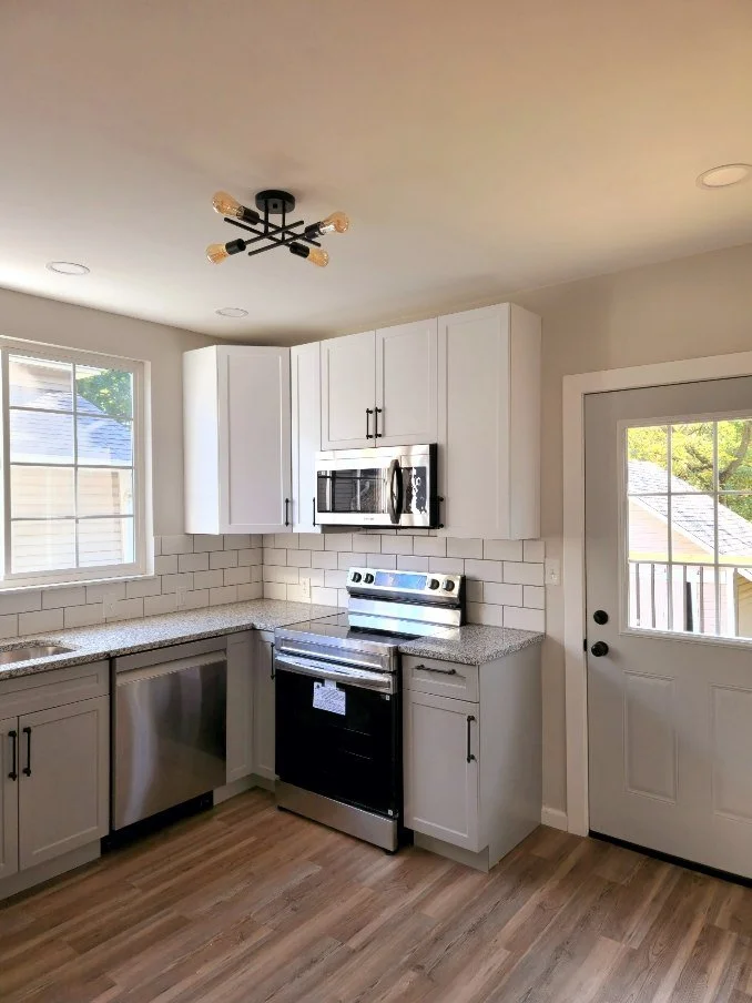 Kitchen: white upper and gray lower cabinets, stainless steel range, microwave and dishwasher, wood-look flooring and a black ceiling light.