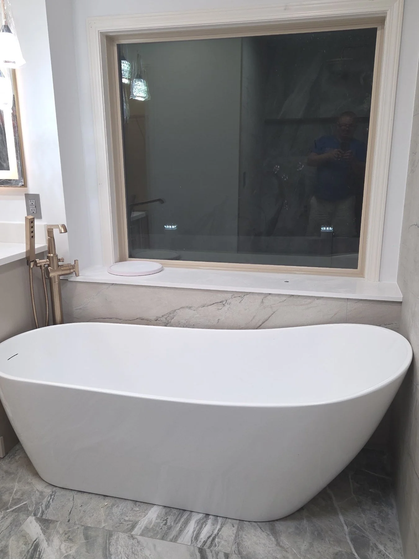 Freestanding tub beneath a window, set against a veined marble-look tile wall.