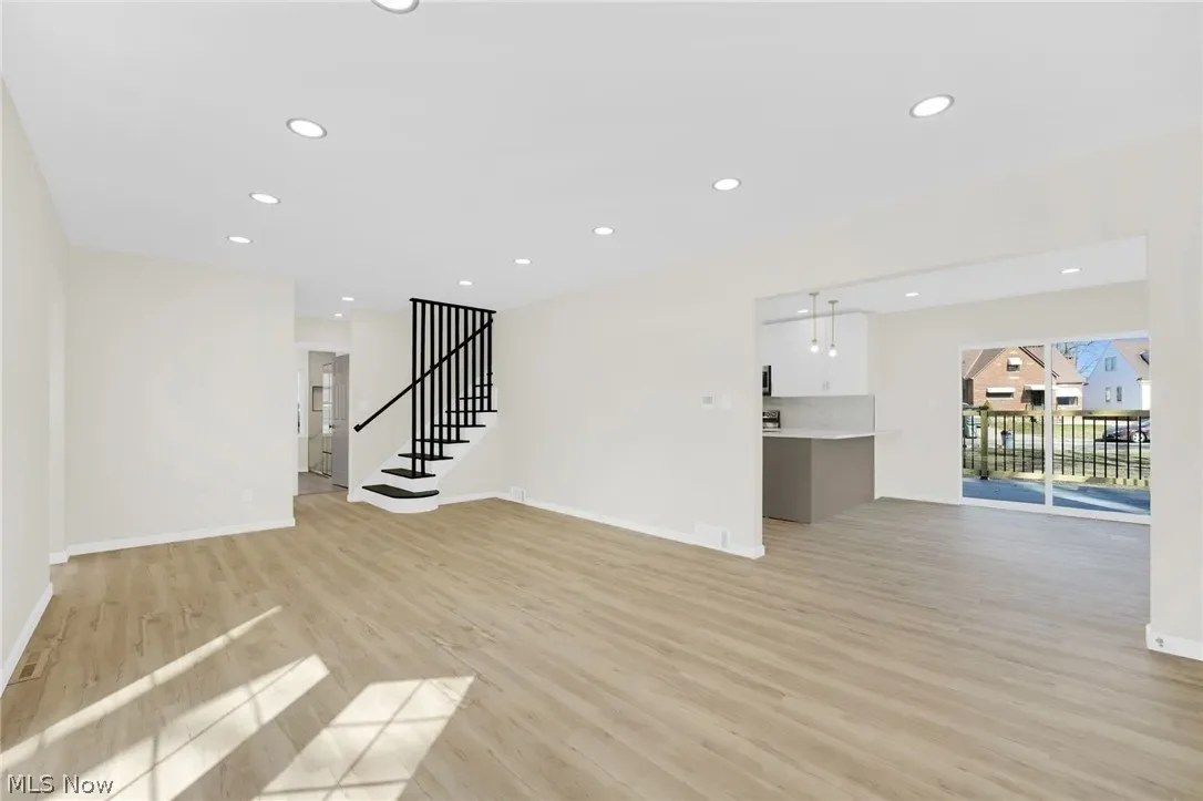 Living room: well-lit space with plank flooring, recessed lighting and a staircase with black balusters.