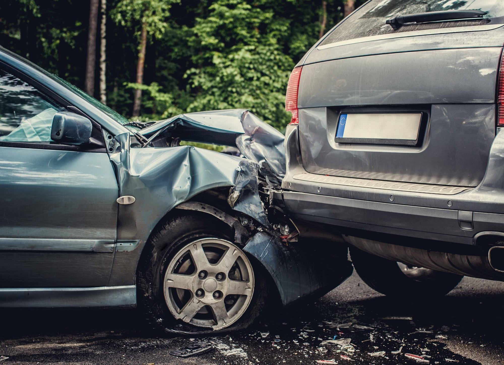 Two cars involved in a rear-end collision, with the front of a silver car crashed into the back of a gray car, causing significant damage to the front of the silver car.