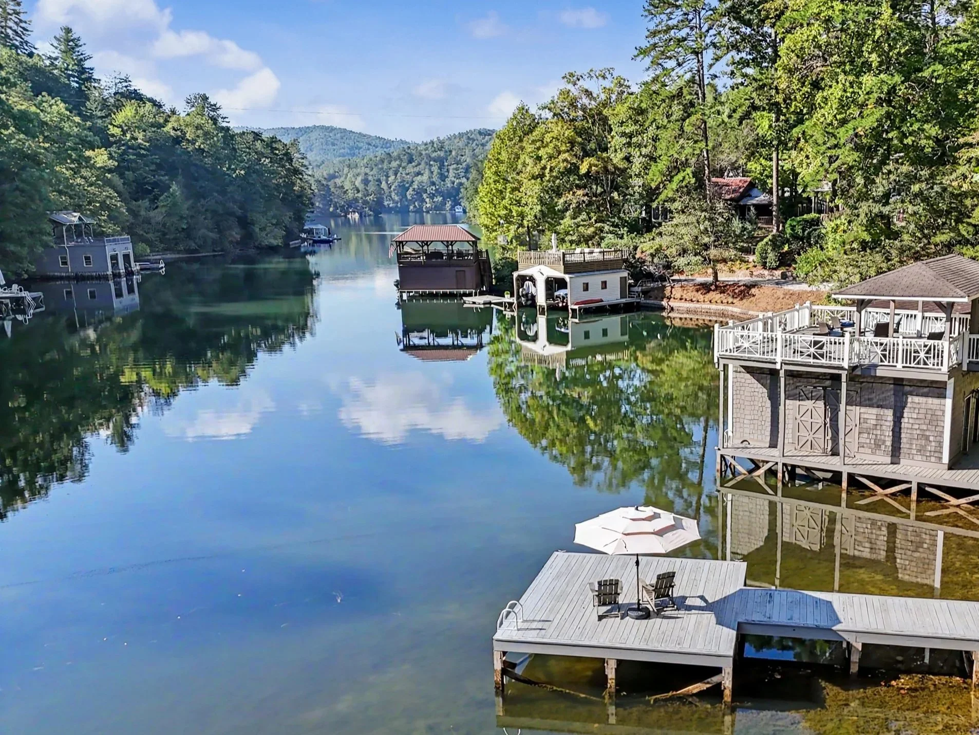 Calm Lake Burton view with houses and docks along the banks, surrounded by lush green trees and forested hills under a clear blue sky.