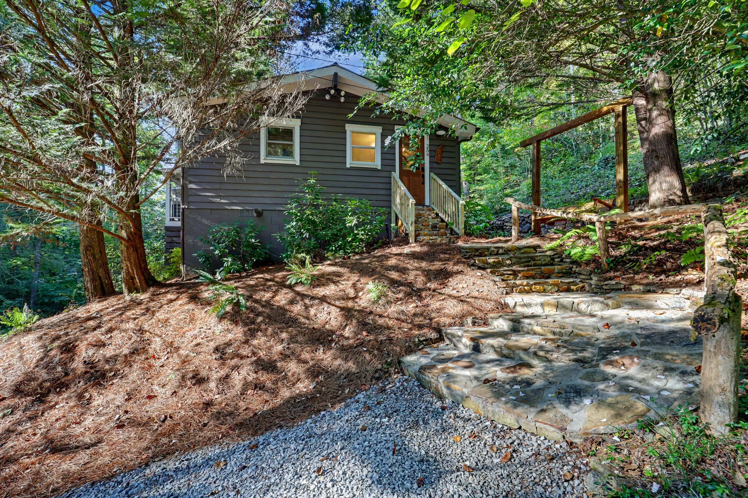 A cozy Lake Burton rental home with white trim surrounded by trees and greenery, with stone steps and a small porch leading to the front door.