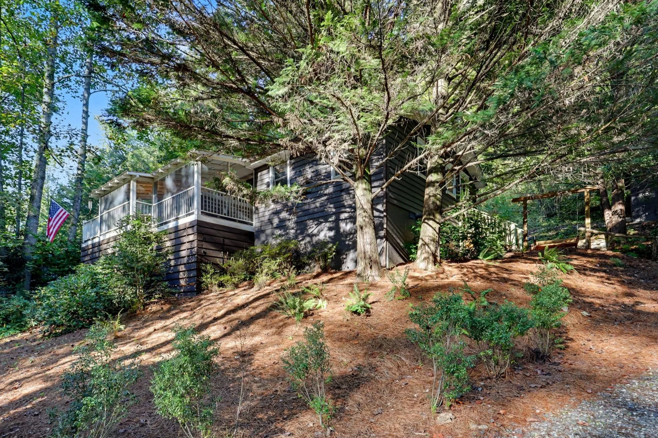 A Lake Burton cabin rental house with a porch surrounded by trees and greenery in a wooded area.