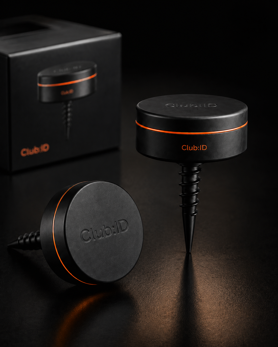 Close-up of two black round devices with orange accents, branded 'Club:ID', placed on a dark surface with a box in the background.