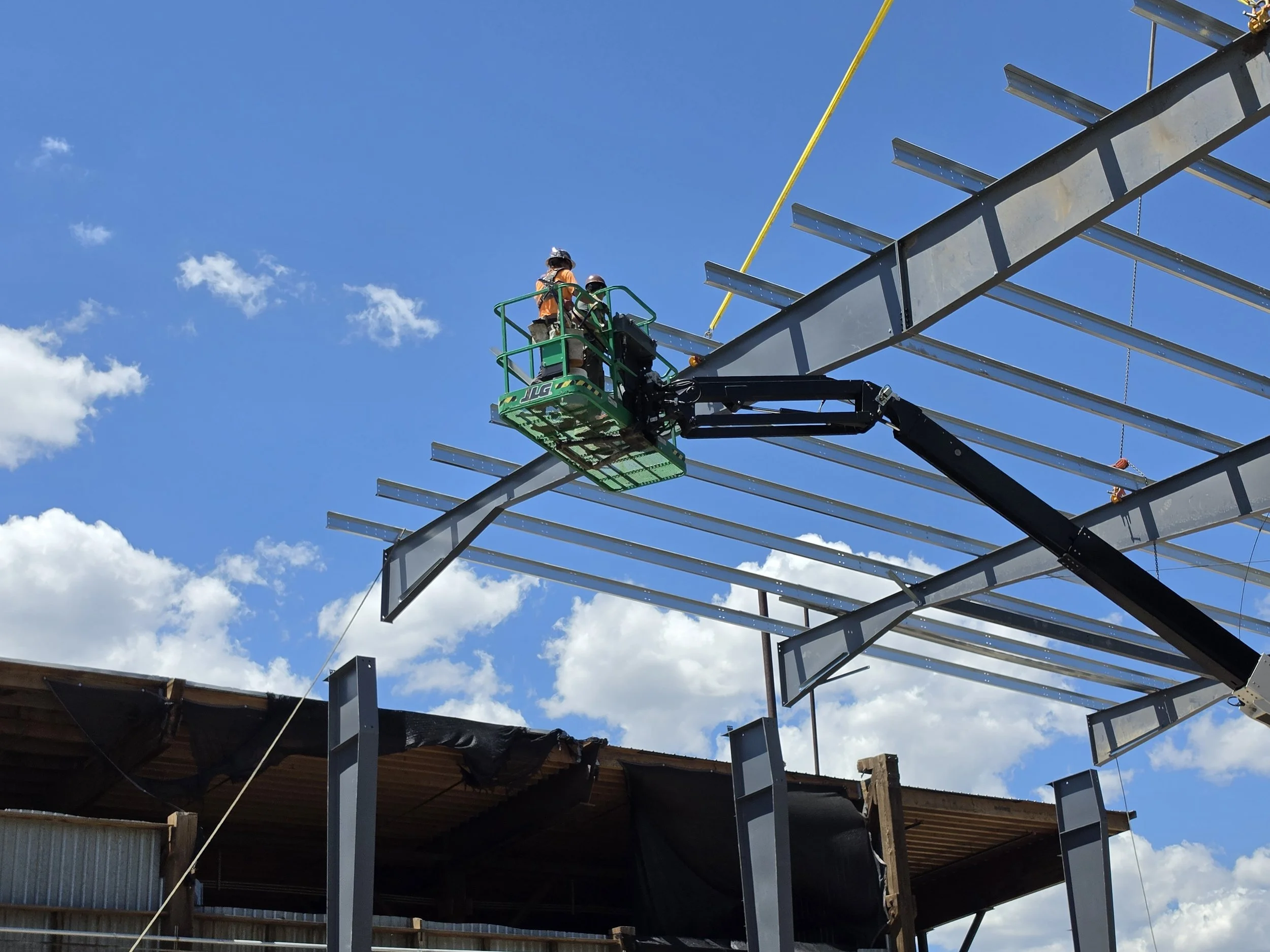 Construction workers on a lift working on a steel structure against a blue sky with some clouds.