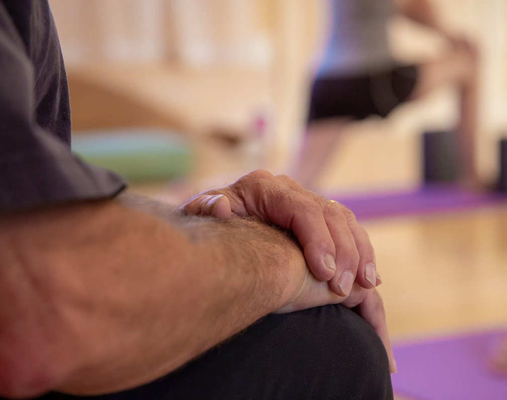A person's hands resting on their knee during a yoga in a studio.