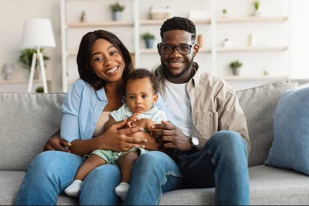 Une famille assise sur un canapé dans un salon moderne, comprenant une femme, un homme et un bébé, tous souriants.
