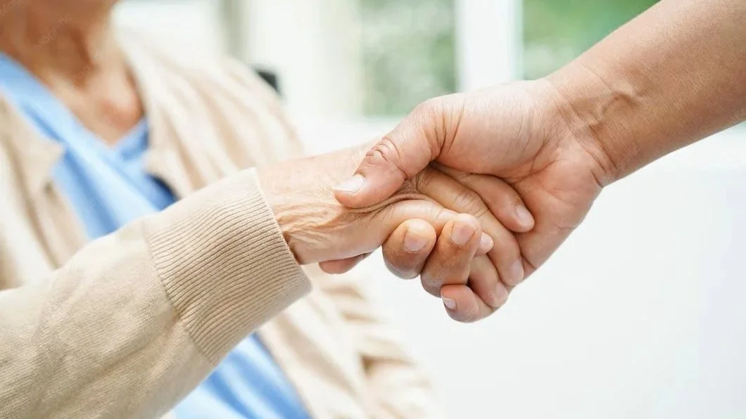 Une poignée de main entre deux personnes, l'une âgée et l'autre plus jeune, dans un environnement lumineux et extérieur.