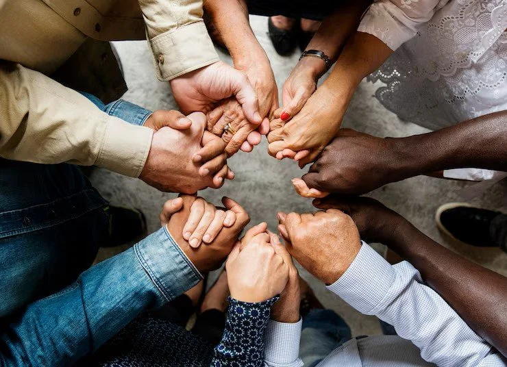 Groupe de personnes de différentes origines tenant leurs mains ensemble en formant un cercle.