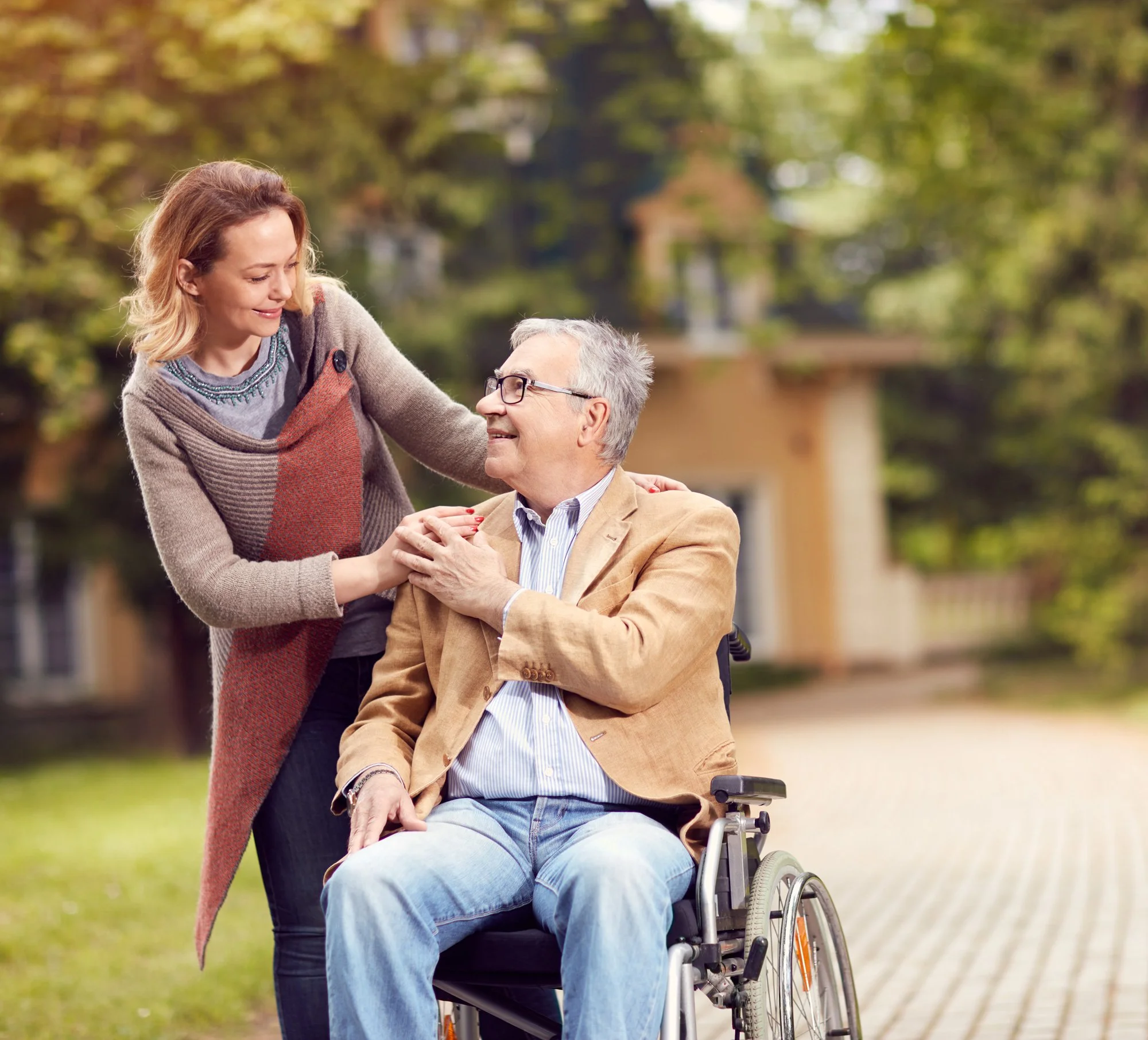 Une femme souriante aide un homme en fauteuil roulant dans un parc pendant l'automne.