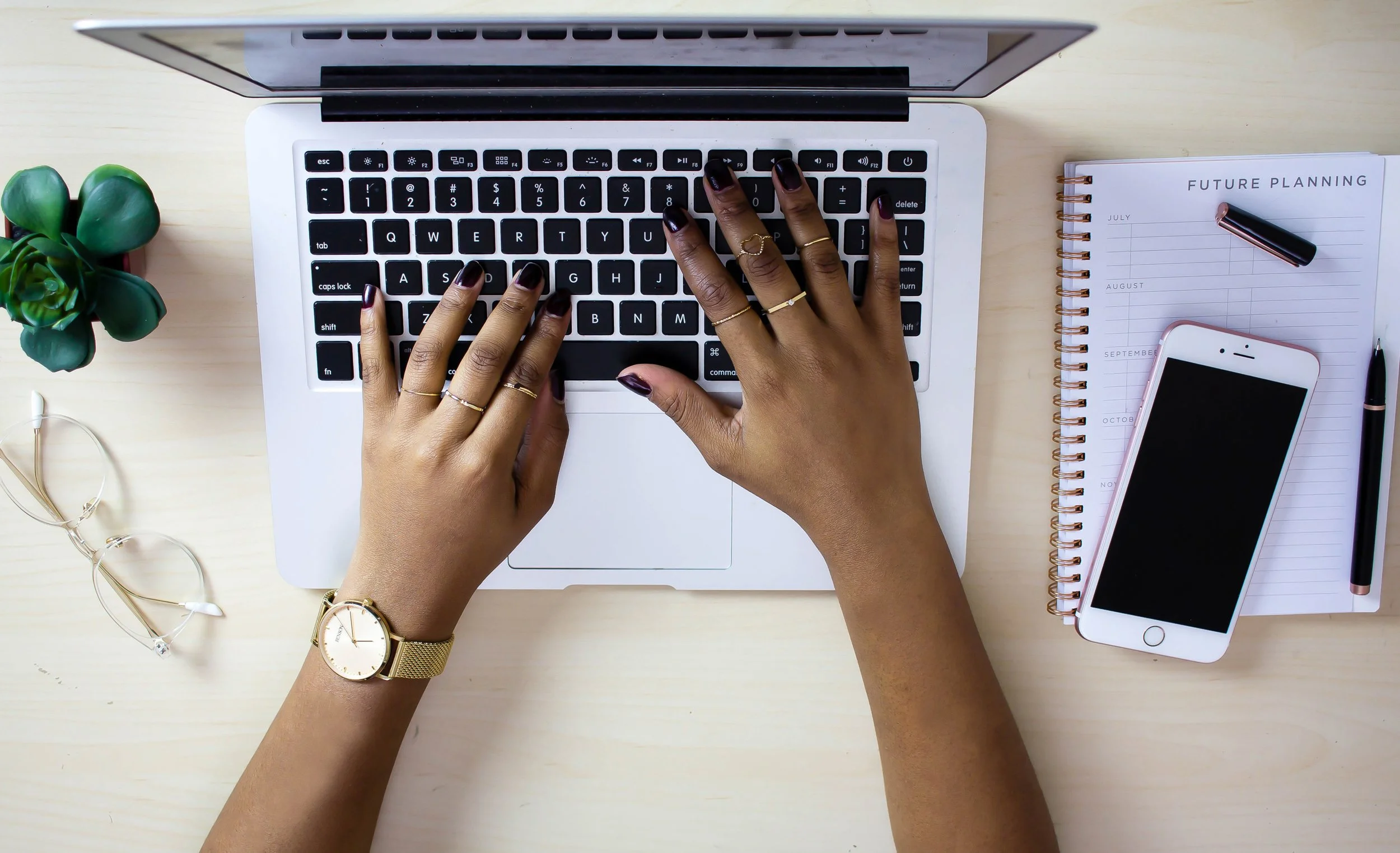 Person typing on a laptop keyboard with a notebook titled 'Future Planning,' a smartphone, and a pen on a desk.