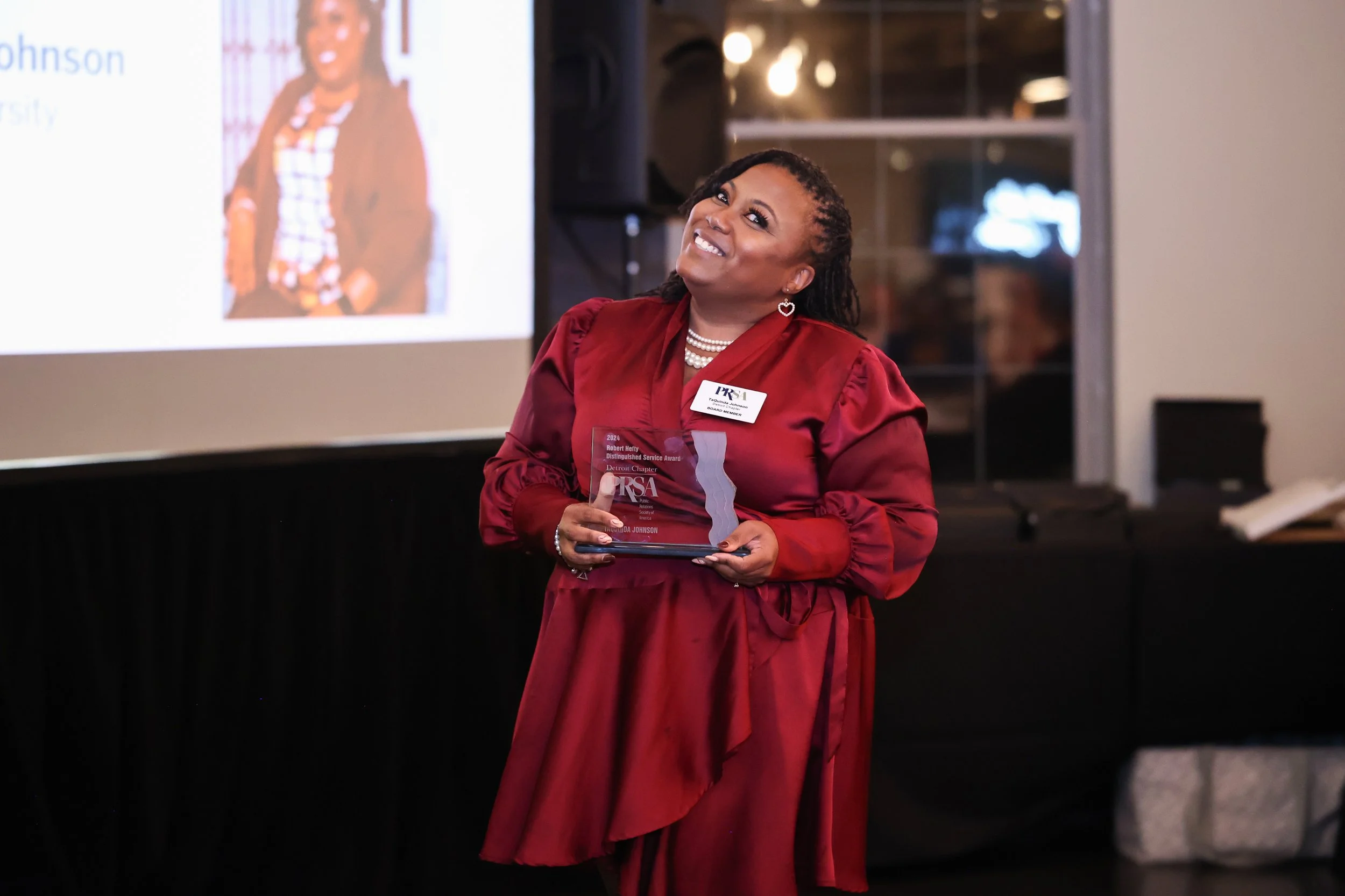 Woman in red dress holding an award at an event with a presentation screen in the background.