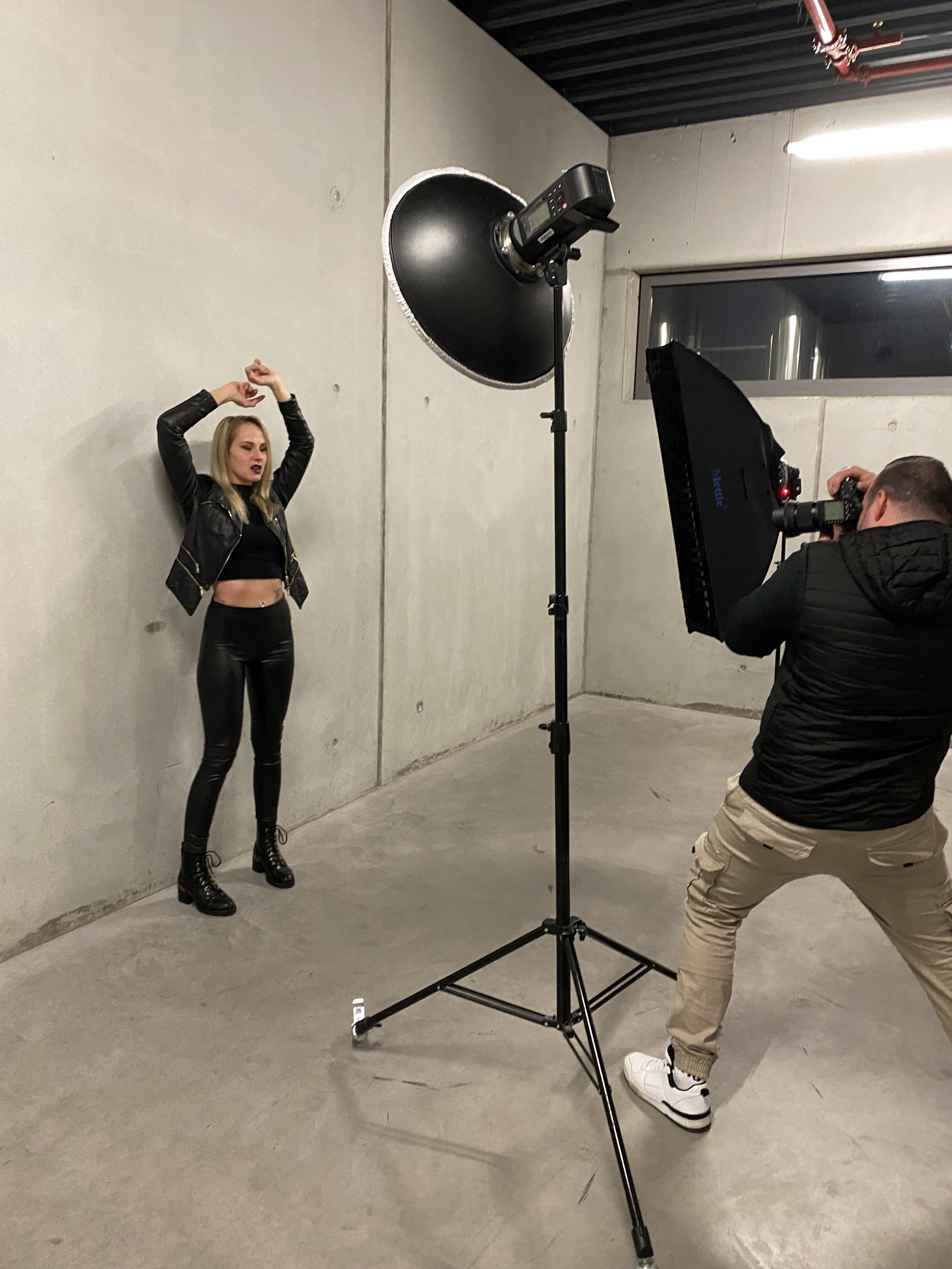 Ein Model posiert vor einer grauen Wand, während ein Fotograf Fotos macht. Die Beleuchtung wird von professionellem Studio-Equipment übernommen.