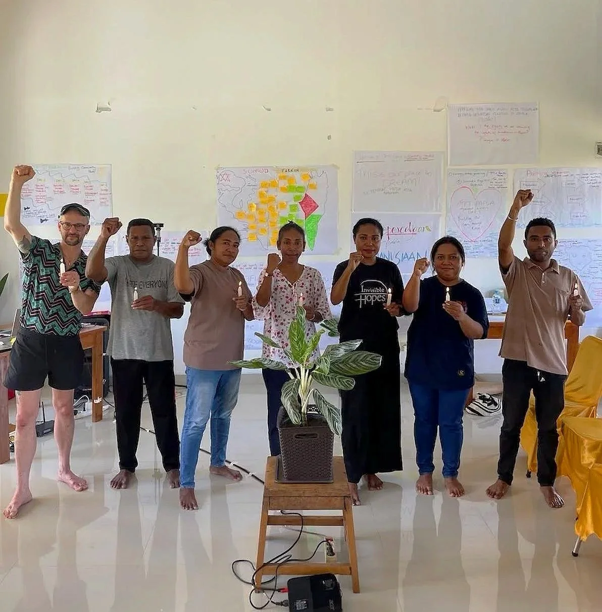 A group standing next to each other holding a lit candle in one hand and having a fist held up