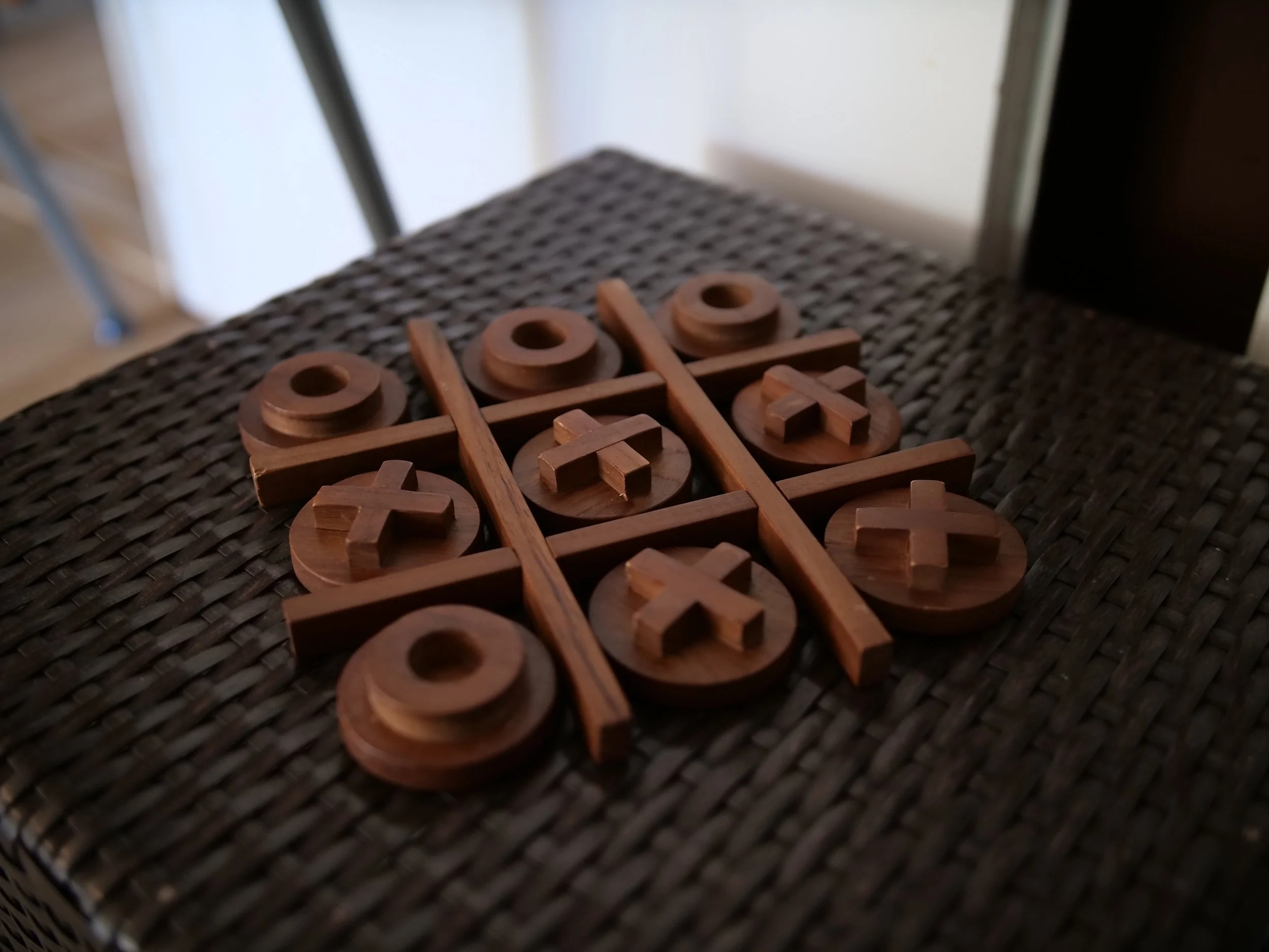 Bord met houten boter-kaas-en-eieren spel op een donkere, gevlochten tafeltje.