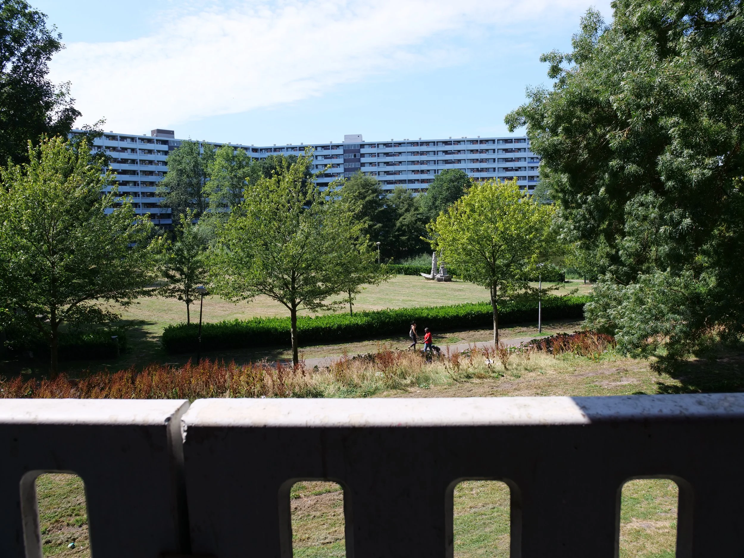 Uitzicht op Gravestein vanuit het balkon van FILAppartement en het park met groene bomen en grasvelden. Twee mensen die wandelen op een pad in het park.