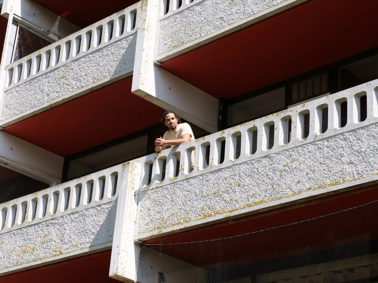 Wouter Pocornie leunend op een balkon in de flat Gledershoofd met een witte betonmuur en rechthoekige kijkgaten in de wand.