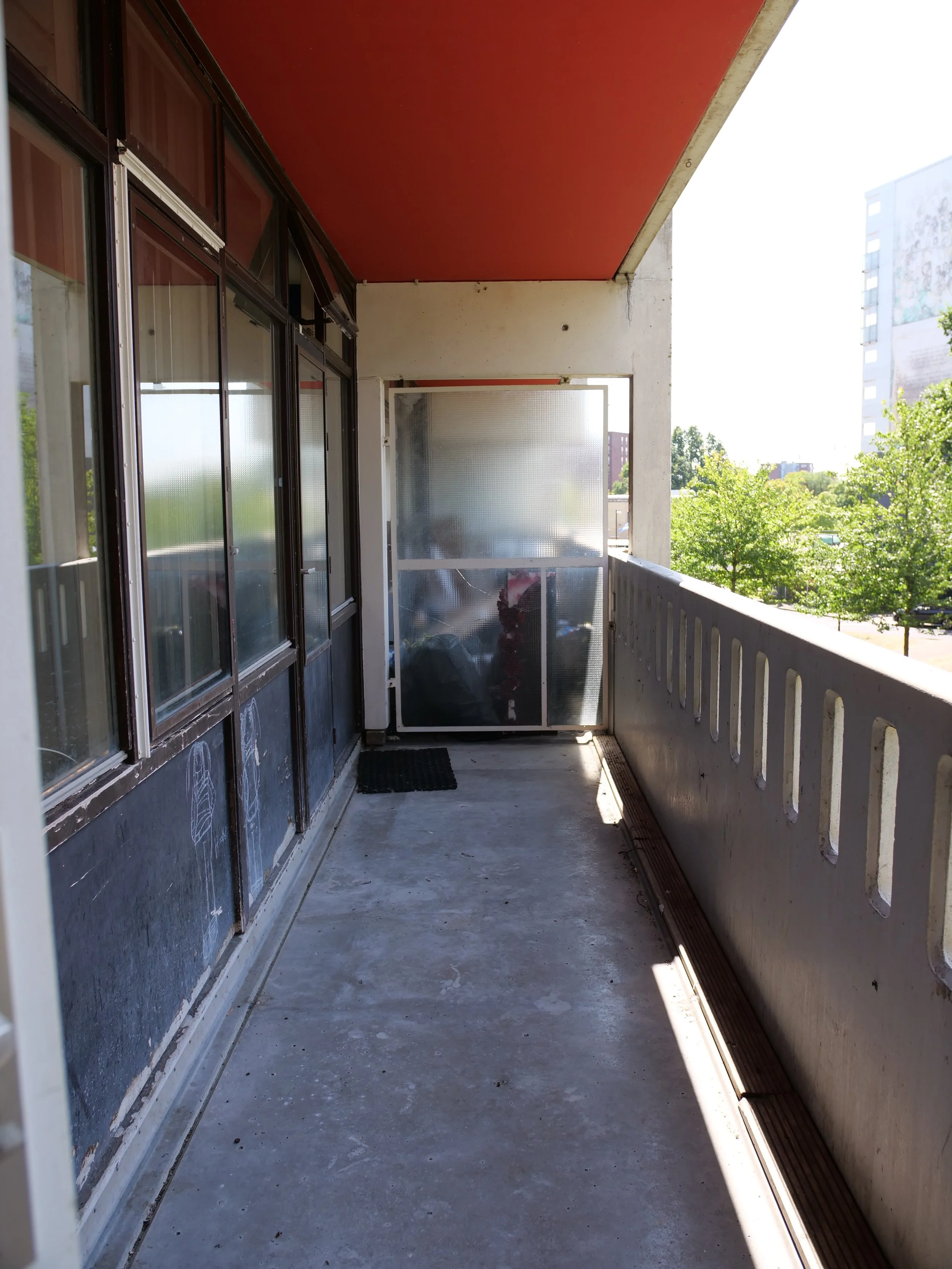 Balkon met glasdeuren en uitzicht op bomen en gebouwen in de verte.