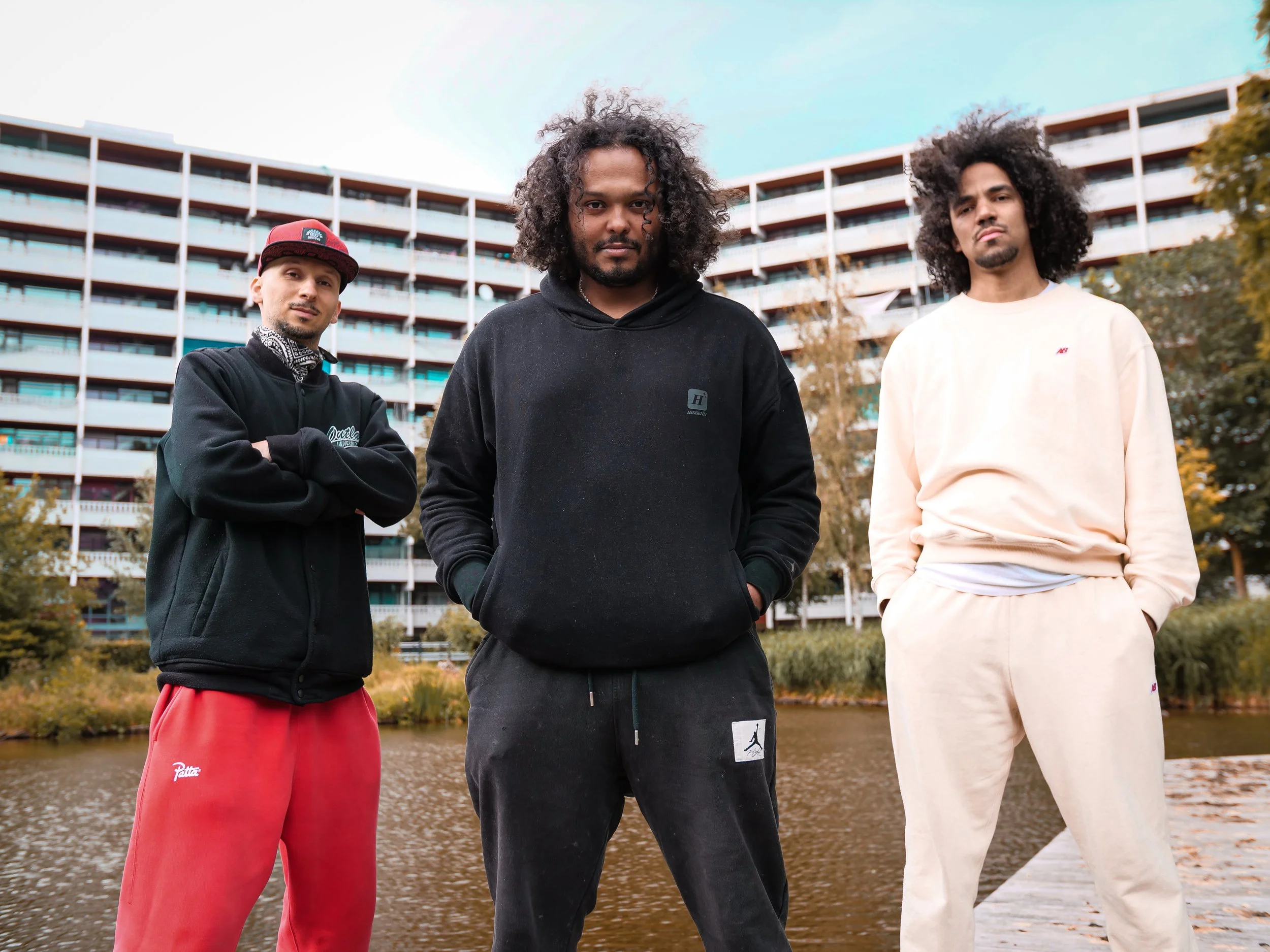 Karim Khamis, Shaquille Veldboom en Wouter Pocornie staan ontspannen voor een rivier, met de flat Geldershoofd op de achtergrond.