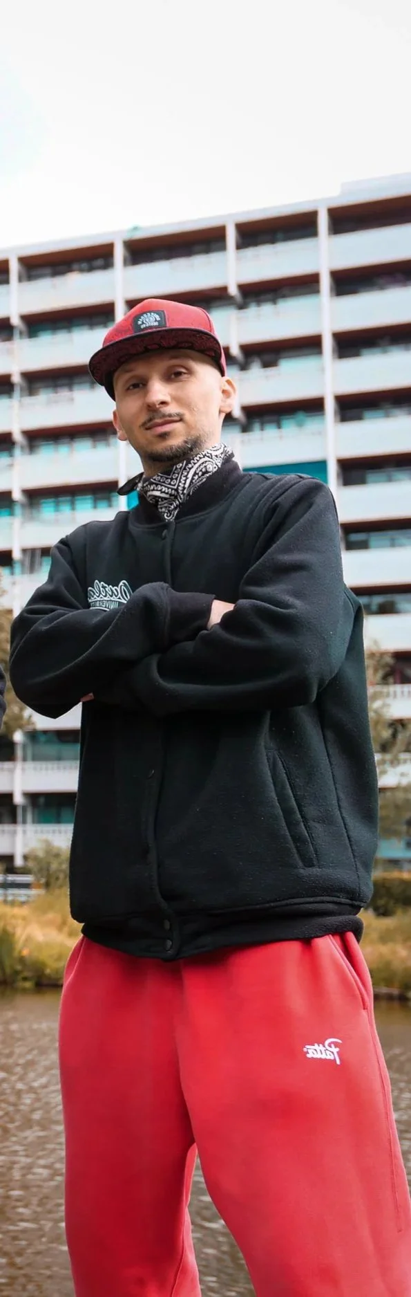Karim Khamis met een rode pet, zwarte jas en rode sweatpants, staat met gekruiste armen voor Geldershoofd.