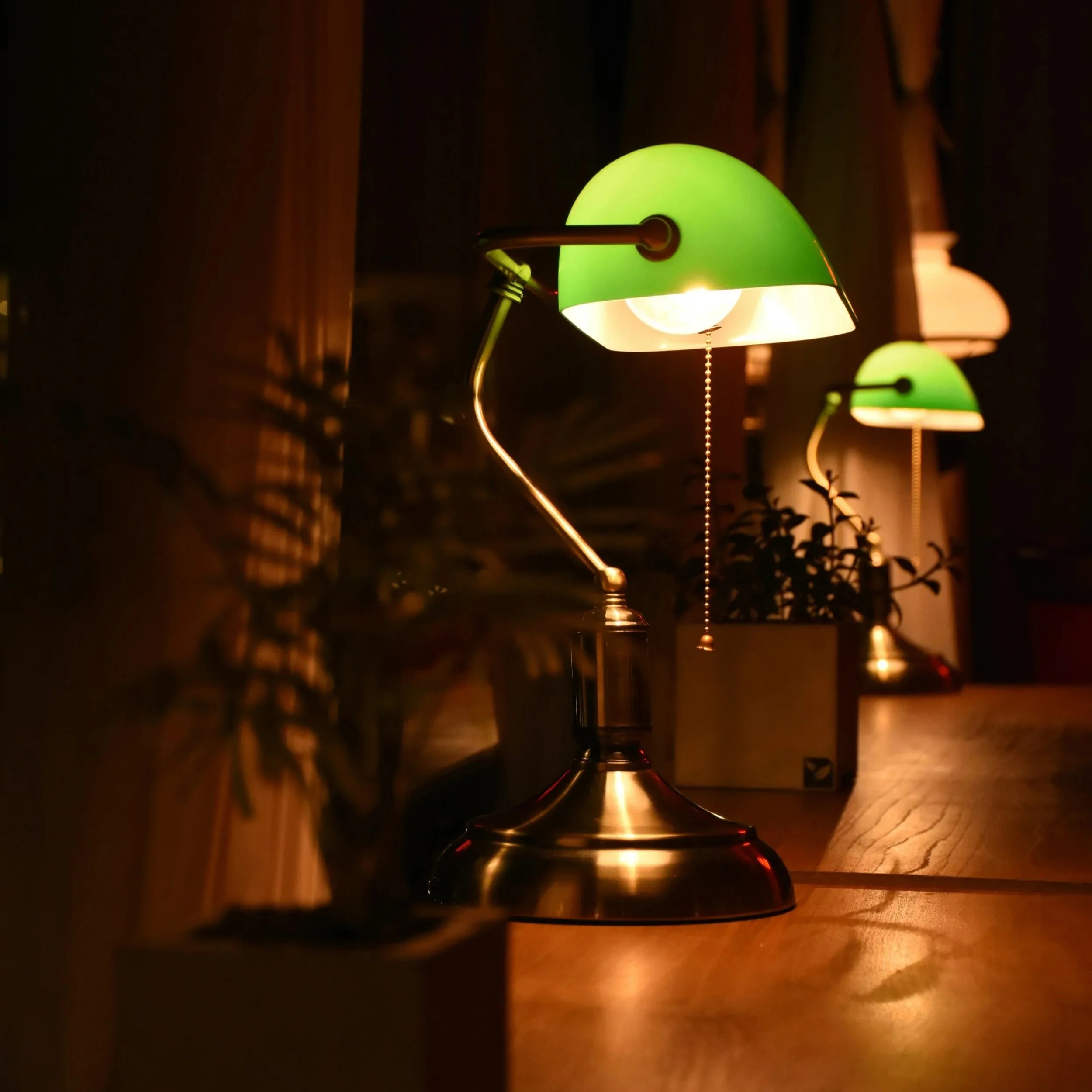 A lit green banker's lamp casting a warm glow across a dark wooden desk.