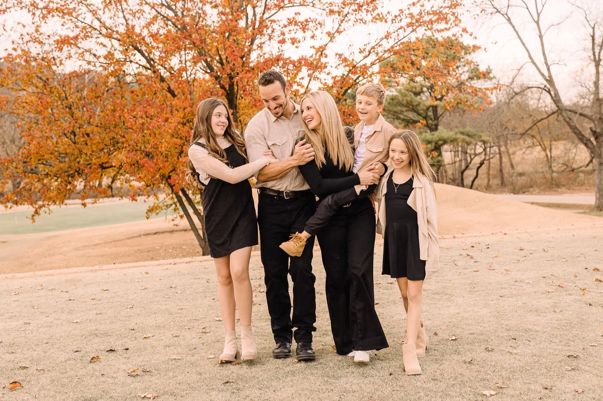 Family of five enjoying an autumn day outdoors, walking on a park path. They are talking and smiling, with vibrant fall leaves and trees in the background.