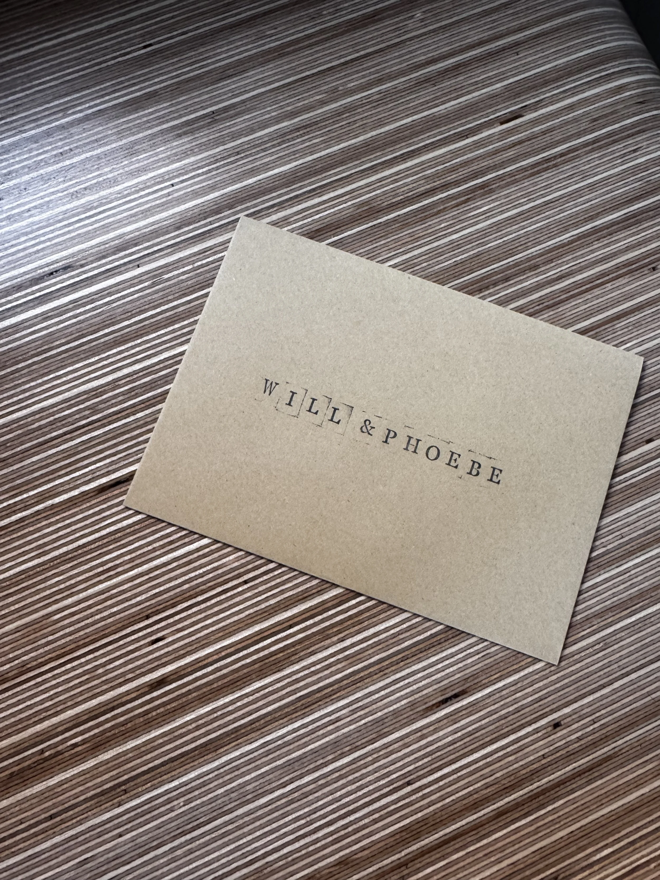 Part of a beige business card with black printed text resting on a wooden surface. Taken by Nook booth Photo Booth