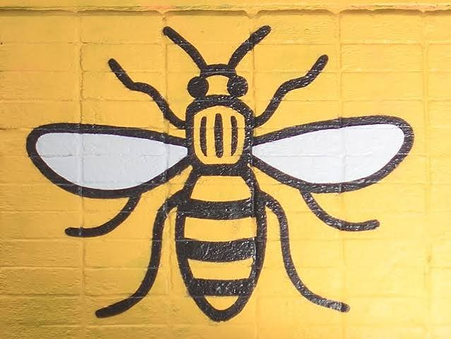 Black graffiti drawing of a bee on a yellow brick wall.