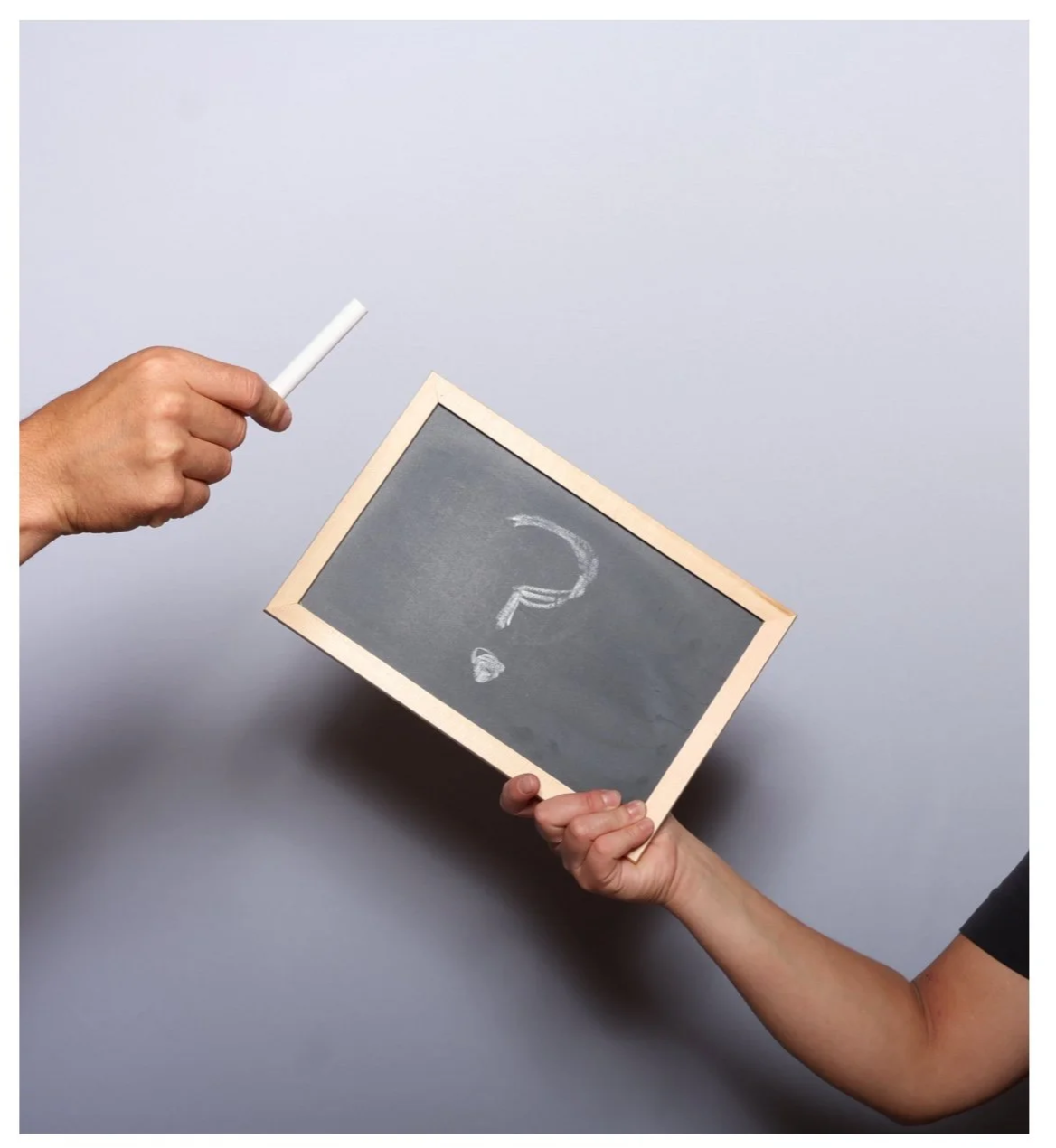 Two hands holding a small chalkboard with a question mark drawn on it and a piece of chalk.