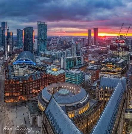 City skyline at sunset with tall skyscrapers, a domed stadium, and cranes in the background.