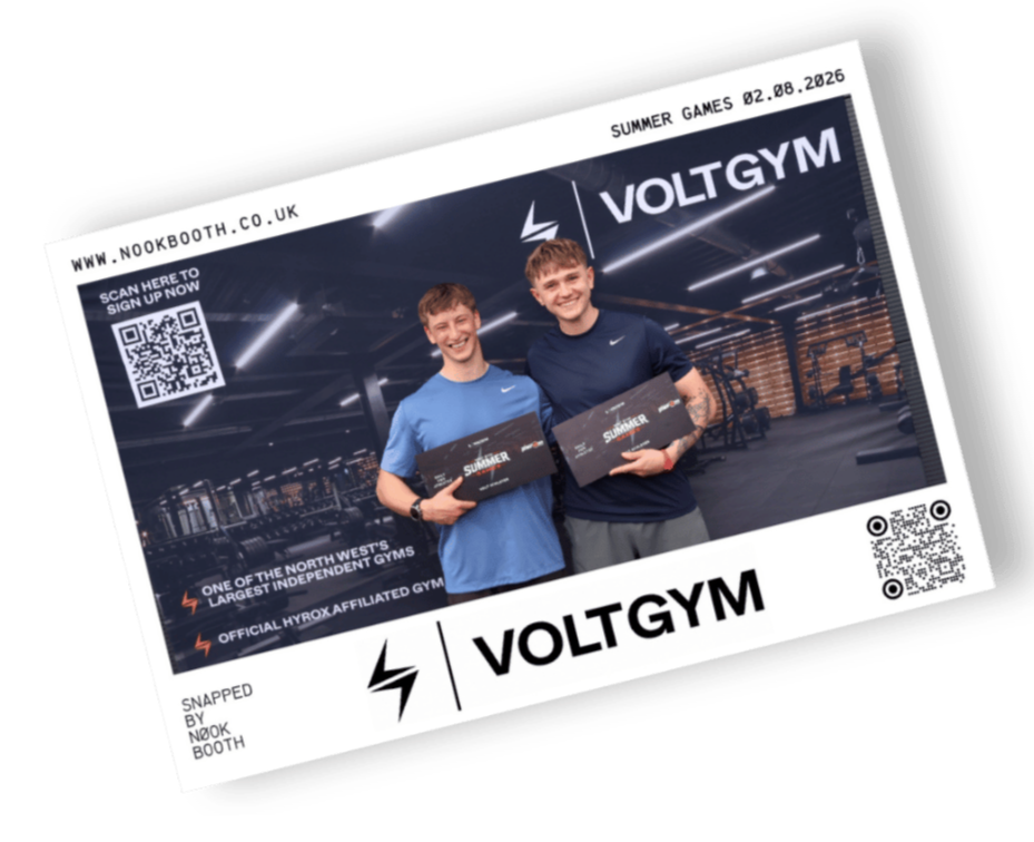 Two young men smiling and holding black boxes in a modern gym with the sign VOLTGYM, gym equipment visible in the background, promotional QR code and website link.