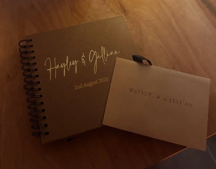 A wedding guest book and an envelope with printed text on a wooden surface. Taken by Nook booth Photo Booth