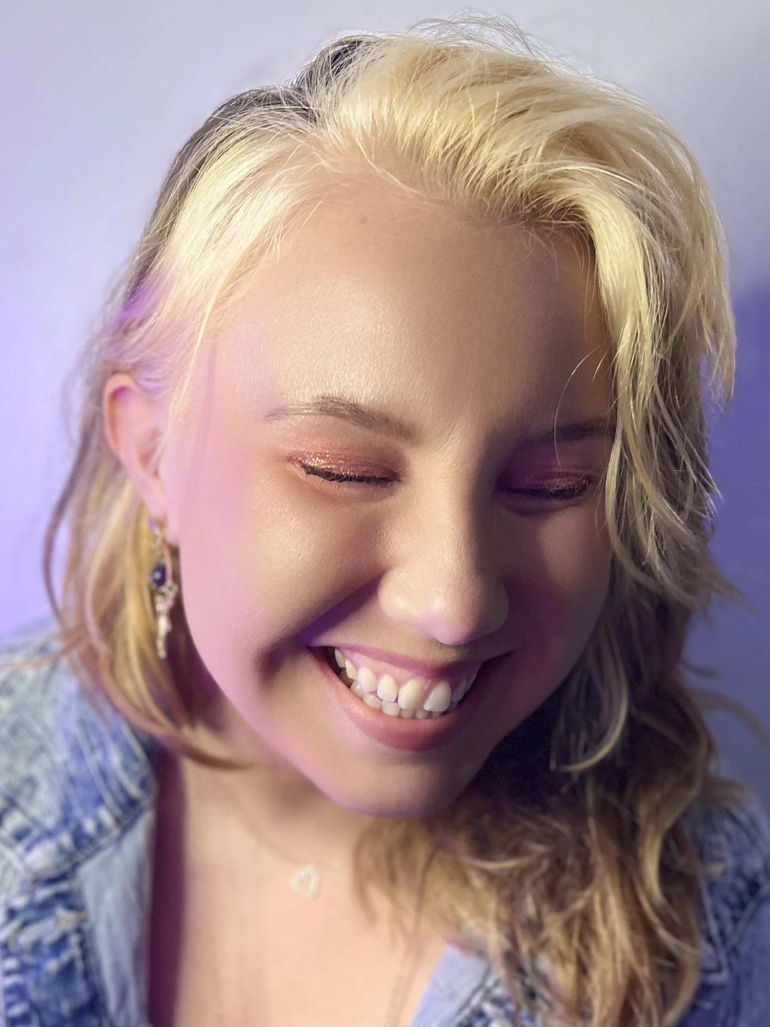 A smiling woman with blonde hair and closed eyes, framed closely.