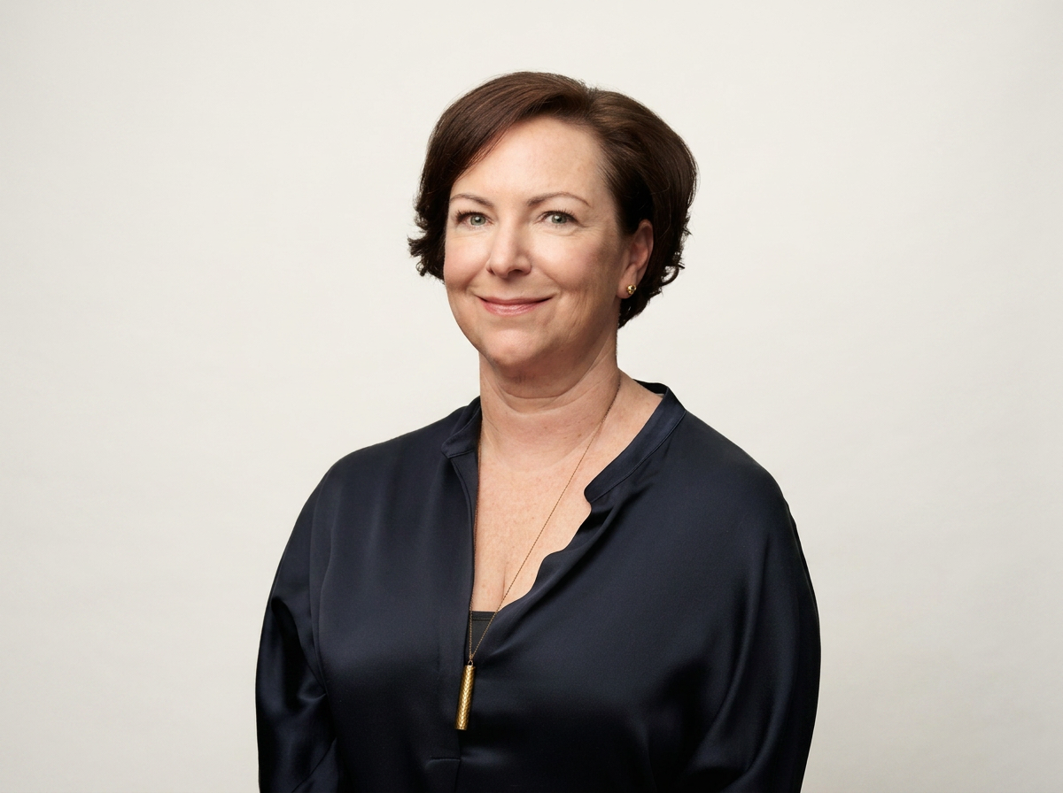 Headshot of a woman with short brown hair, wearing a black blouse and a gold pendant necklace, smiling slightly against a plain light background.