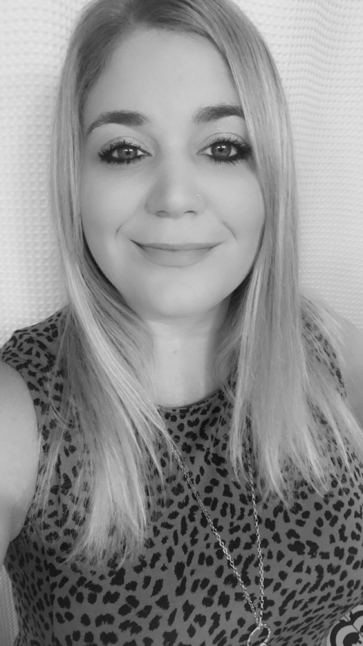 Black and white portrait of a smiling woman with long, straight hair and light-colored eyes, wearing a leopard print top and a necklace.