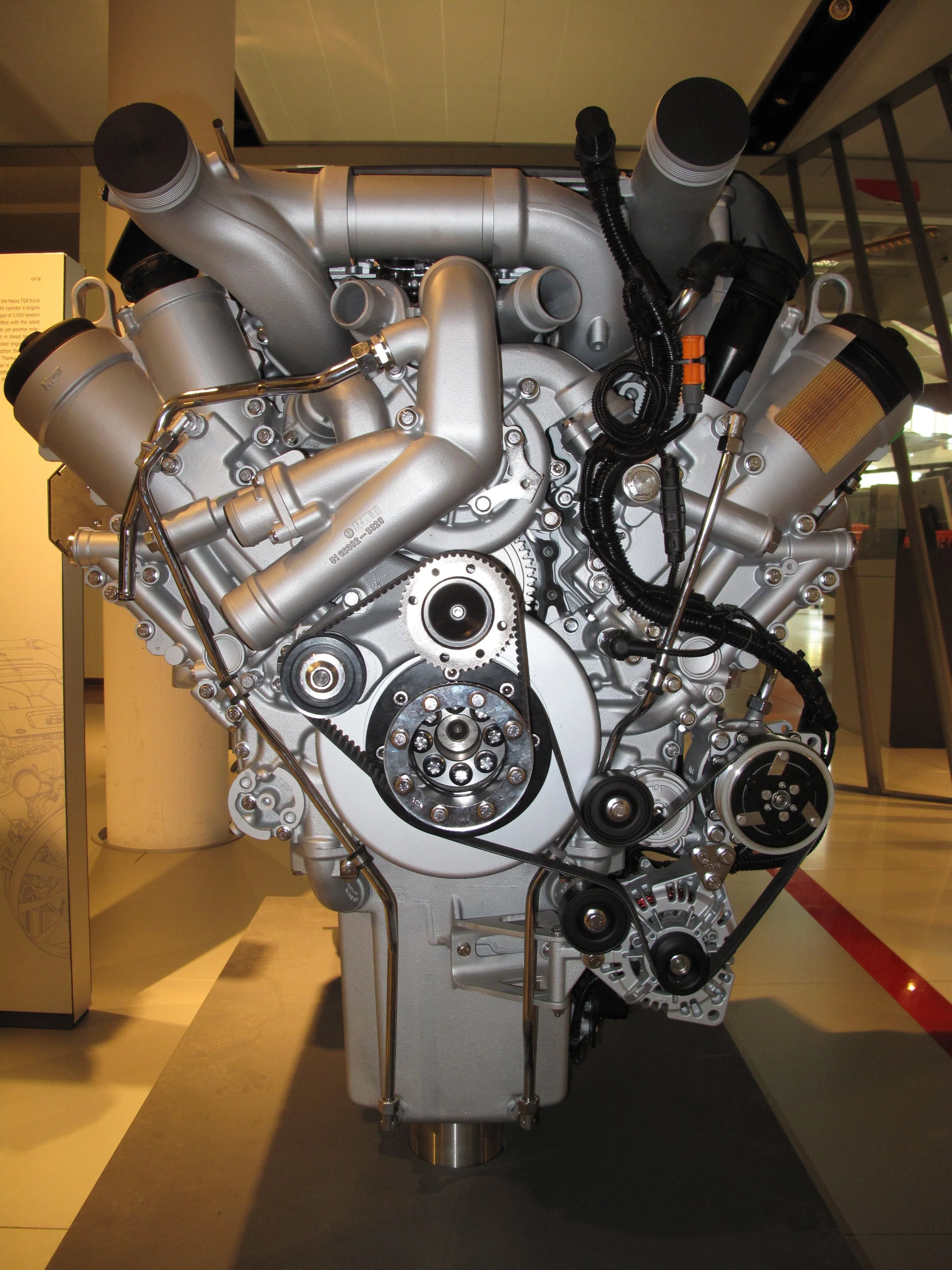 A large, silver automotive engine on display in a museum or exhibition setting.