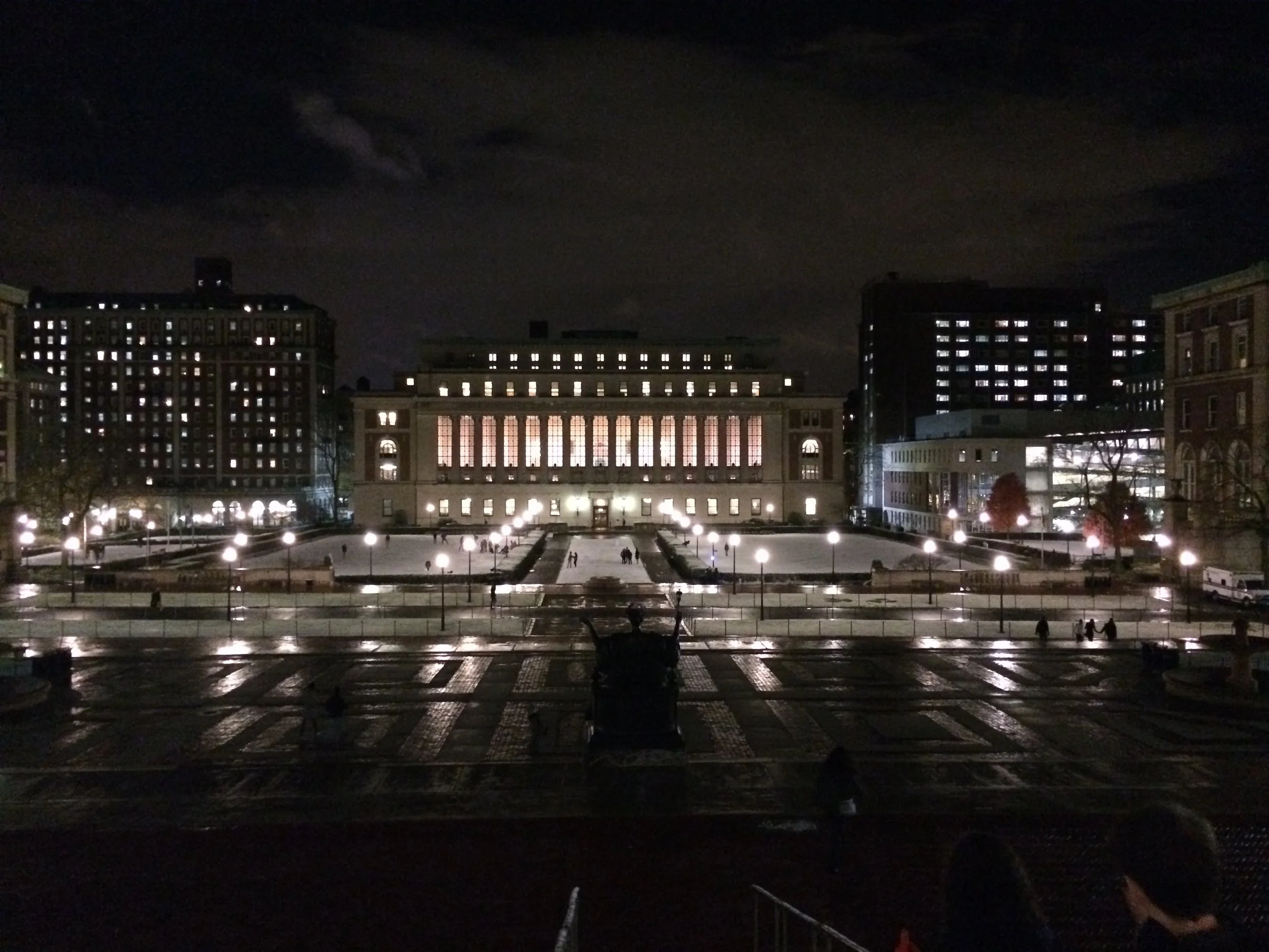 Nighttime cityscape with illuminated buildings and a fountain area in the foreground. Columbia University, Morningside Heights, New York City, NYC
