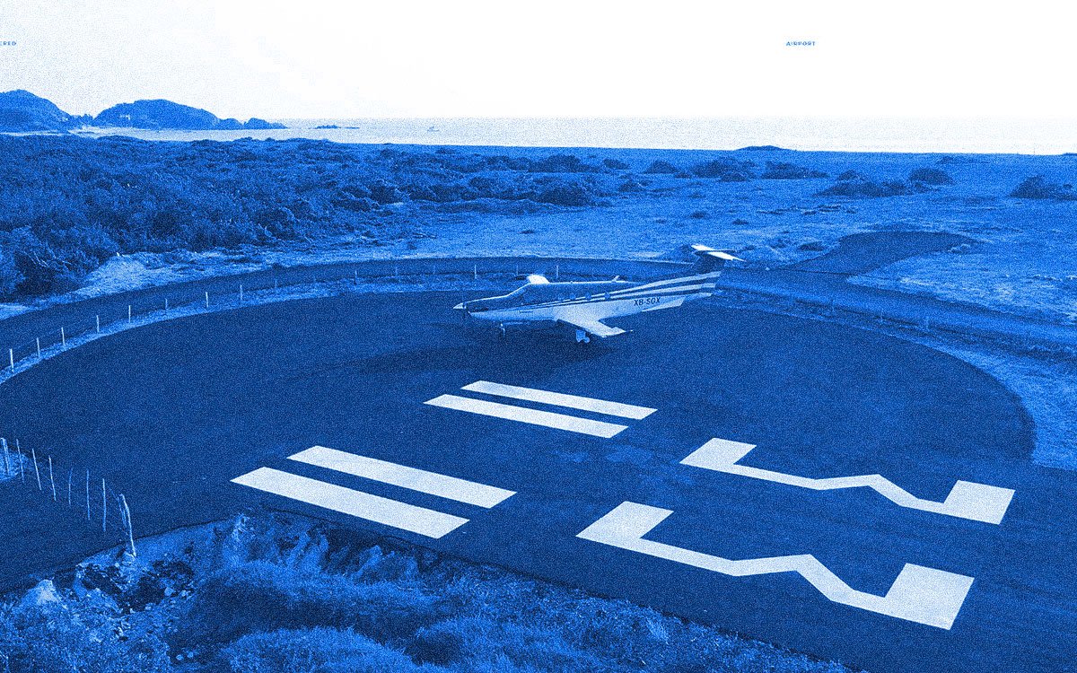A small airplane on a helipad near a coastal area with hills in the background.