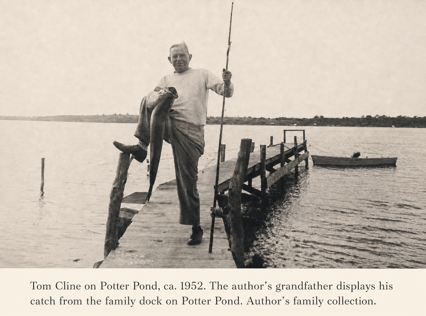 An elderly man stands on a wooden dock holding a large fish in one hand and a fishing rod in the other, with a small boat docked nearby on a calm body of water.
