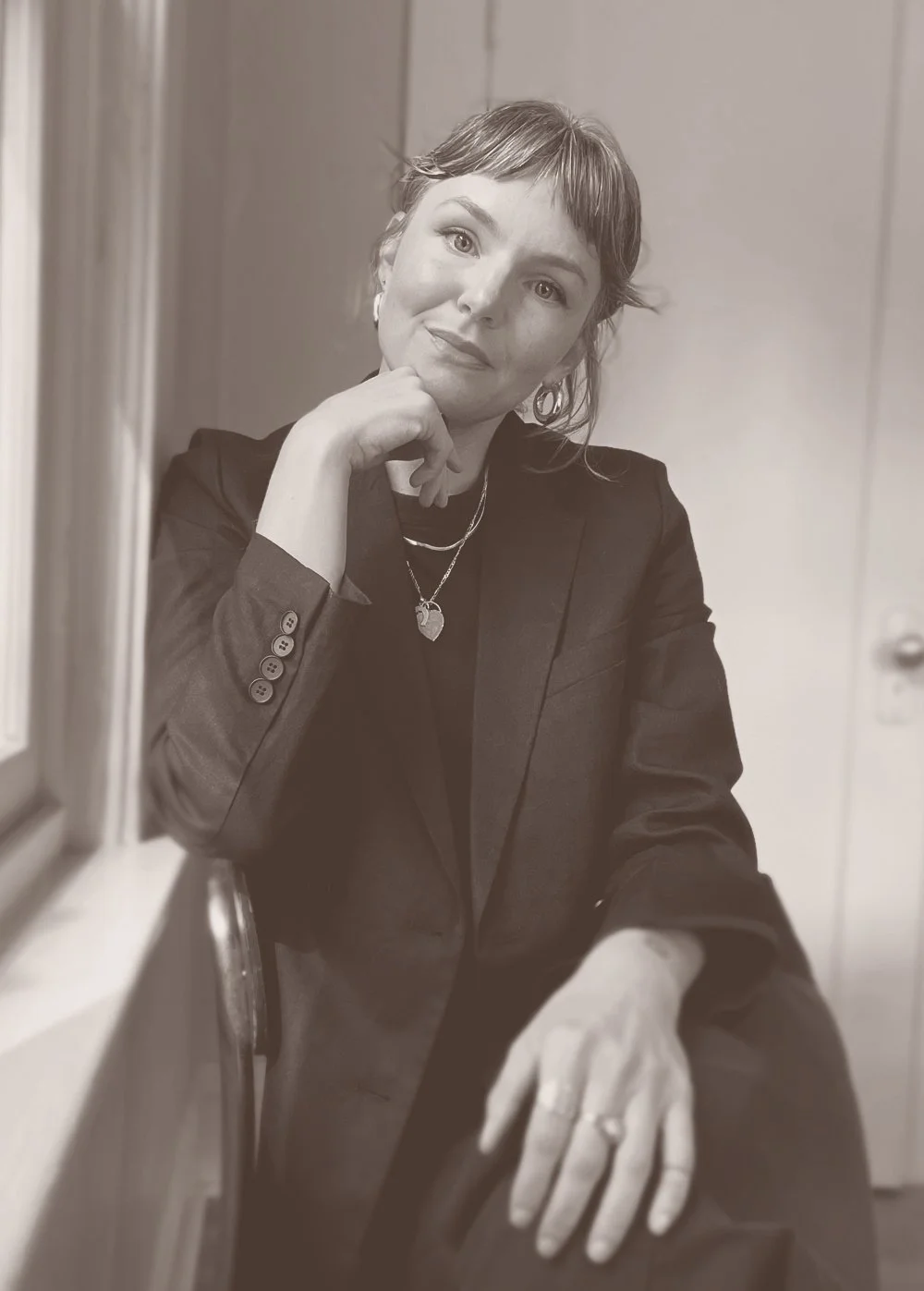 Woman sitting, smiling softly, resting chin on hand.