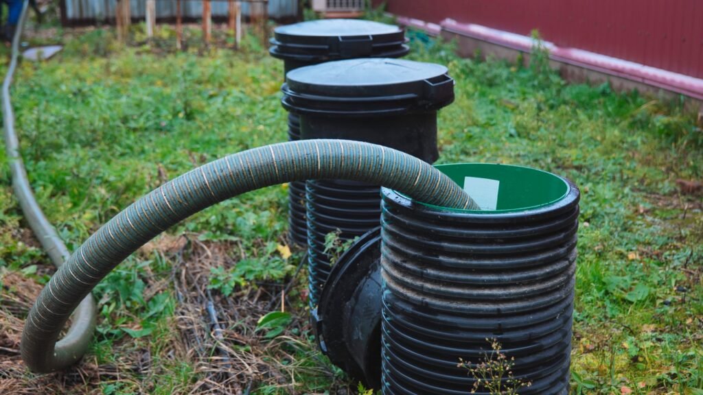 Close-up of a series of underground utility manholes in a grassy yard, with a flexible green hose connected to one of them.