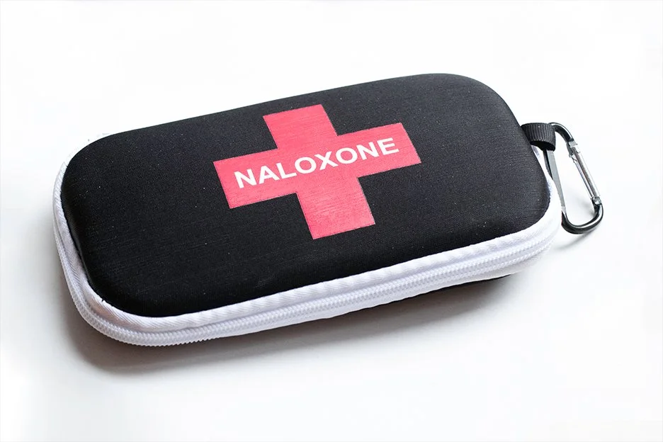 Black carrying case with a pink medical cross and the word "NALOXONE" printed on it, attached to a carabiner clip.