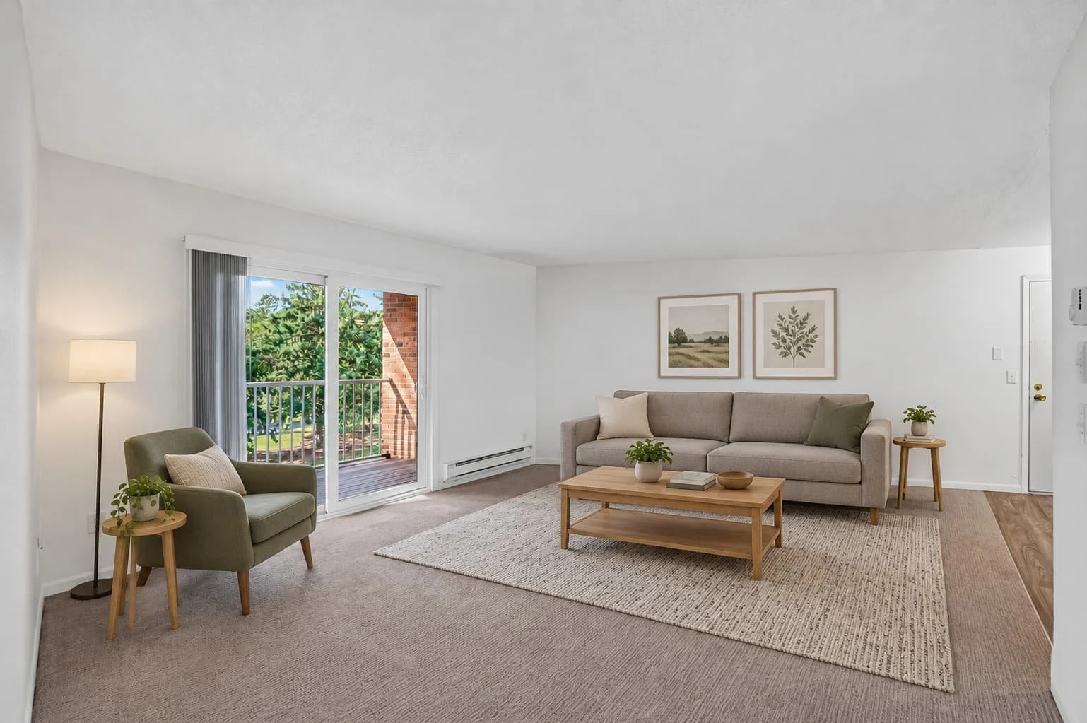 Living room with white walls, beige sofa, green armchair, wooden coffee table, sliding glass door leading to balcony, and various framed artwork on the wall.