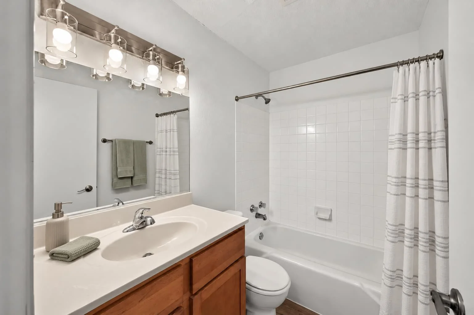 A clean bathroom with a vanity sink, mirror, light fixture, toilet, bathtub with tiled wall, and striped shower curtain.