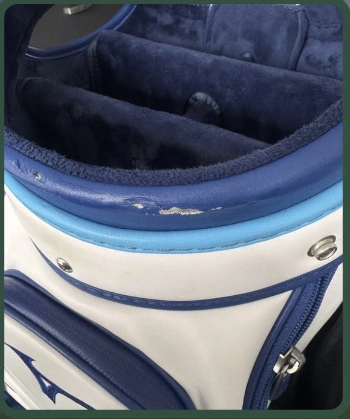 Close-up of a blue and white sports bag, with a damaged zipper and torn fabric, showing a navy blue interior.