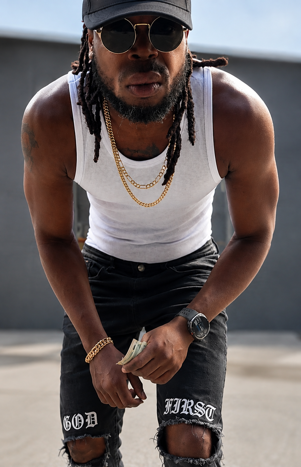 A man wearing a black cap and sunglasses, a white tank top, gold chains, a gold bracelet, a watch, and ripped black jeans with white lettering, holding a stack of cash in his hand. Hookman Bout his business