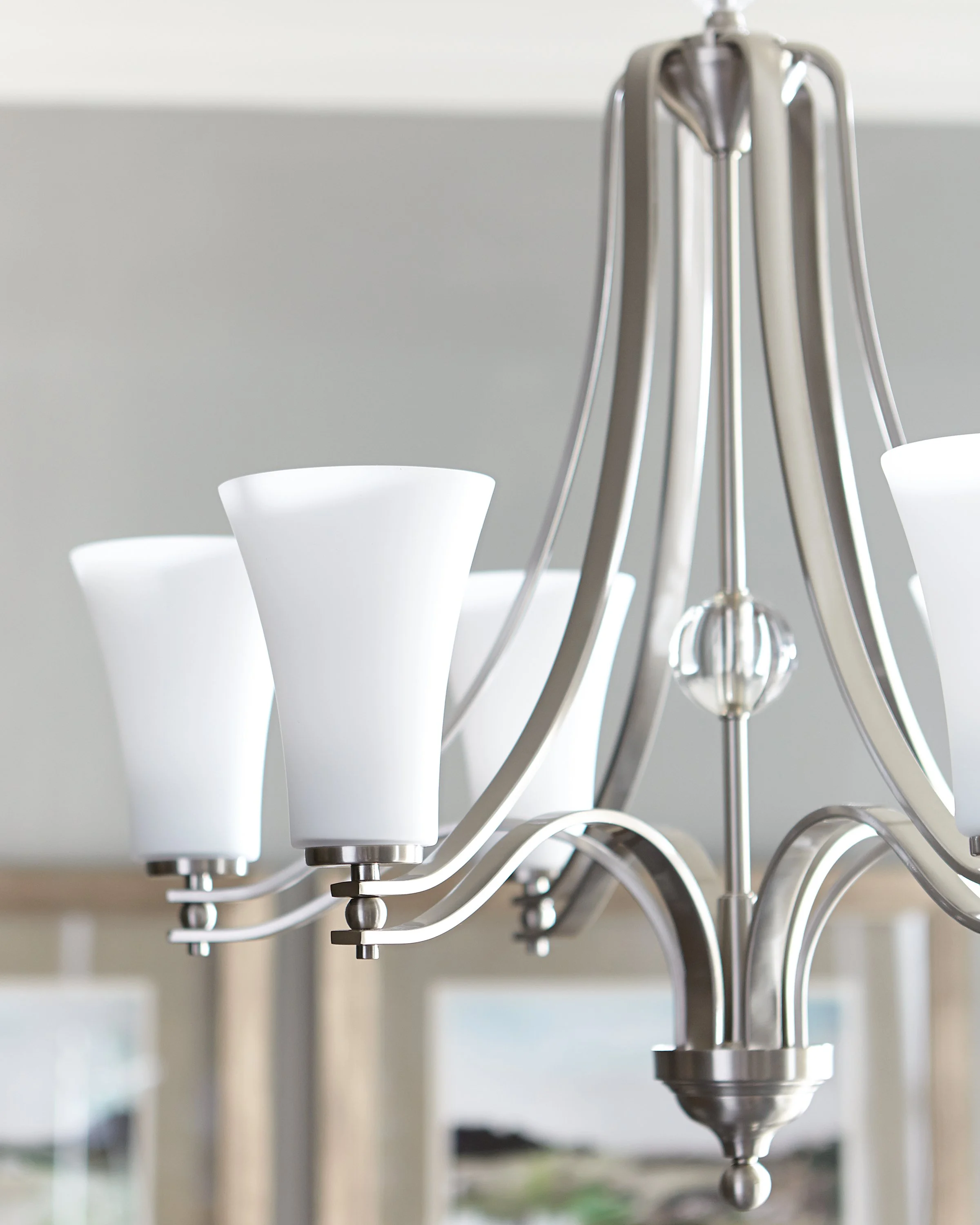 Close-up of a modern chrome chandelier with white frosted glass shades in a bright interior